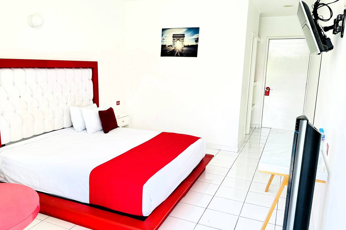 A hotel room with a large bed, white walls, and a red accent wall.