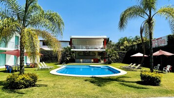 Una piscina al aire libre, sombrillas, sillones reclinables de piscina