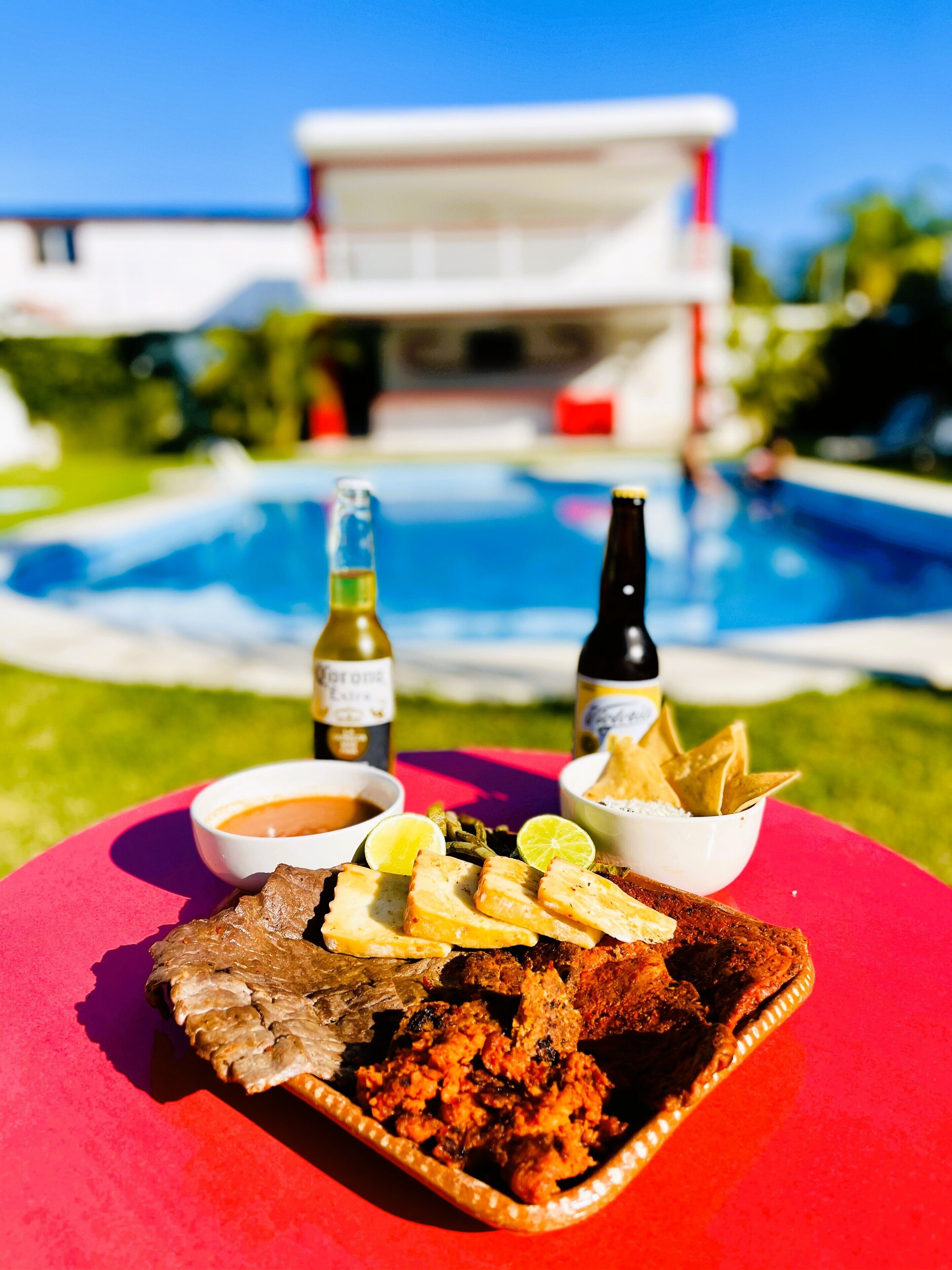 A dining table with a meal, two bottles of beer, and a pool in the background.