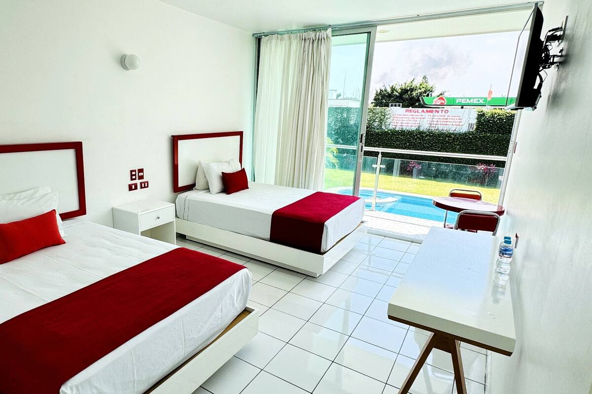 A hotel room with two beds, a small table, and a view of a swimming pool.