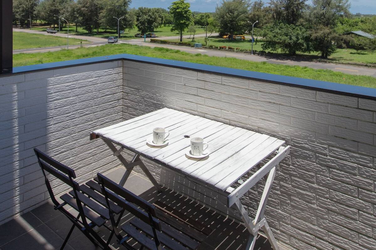 Ein Balkon mit Tisch und Stühlen, der auf eine grüne Landschaft mit Bäumen und einem klaren Himmel blickt.