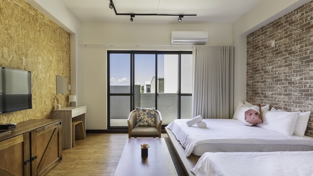 Une chambre d’hôtel avec un plancher en bois, un téléviseur à écran plat, un canapé, un lit avec une literie blanche et une grande fenêtre donnant sur un paysage agréable.