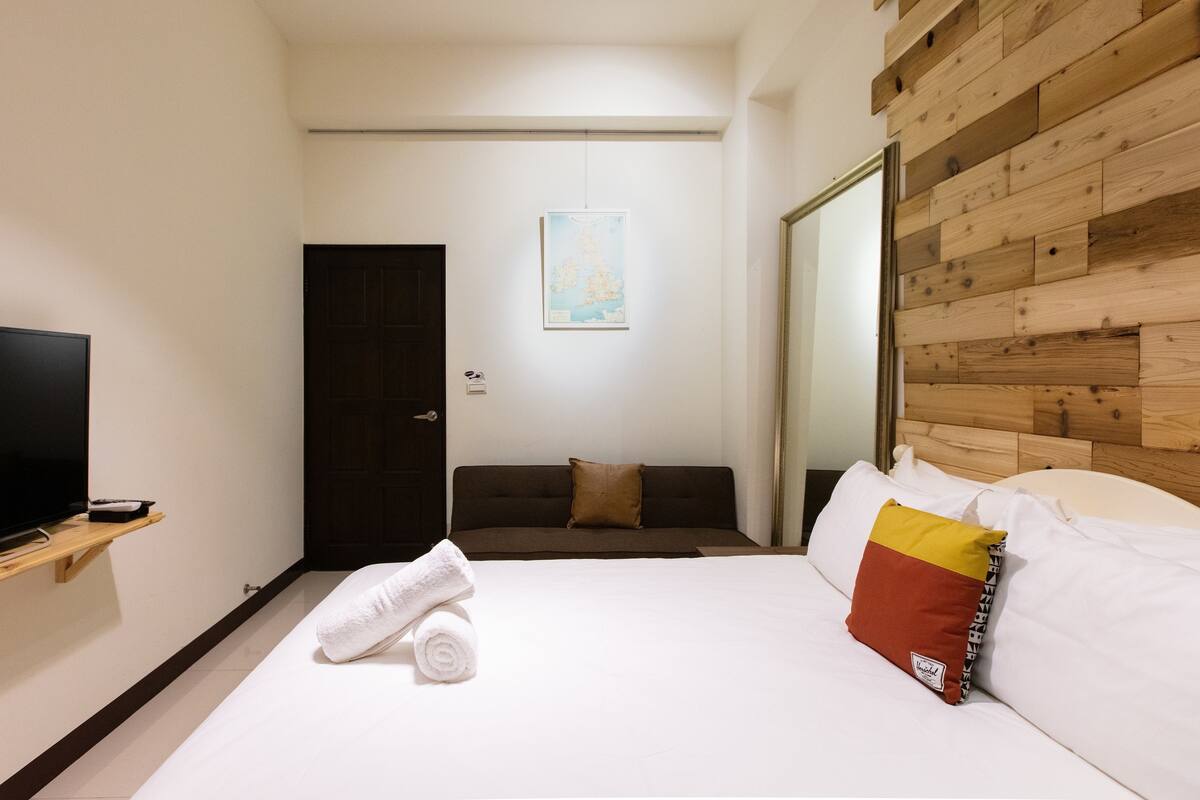 Ein Hotelzimmer mit Bett, Fernseher auf einem Tisch, Holz-Kopfteil und einer Tür.