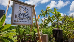 Une enseigne pour l’auberge de jeunesse Happy Hostel, avec un motif représentant un oiseau et un vélo, le tout entouré d’une végétation luxuriante.