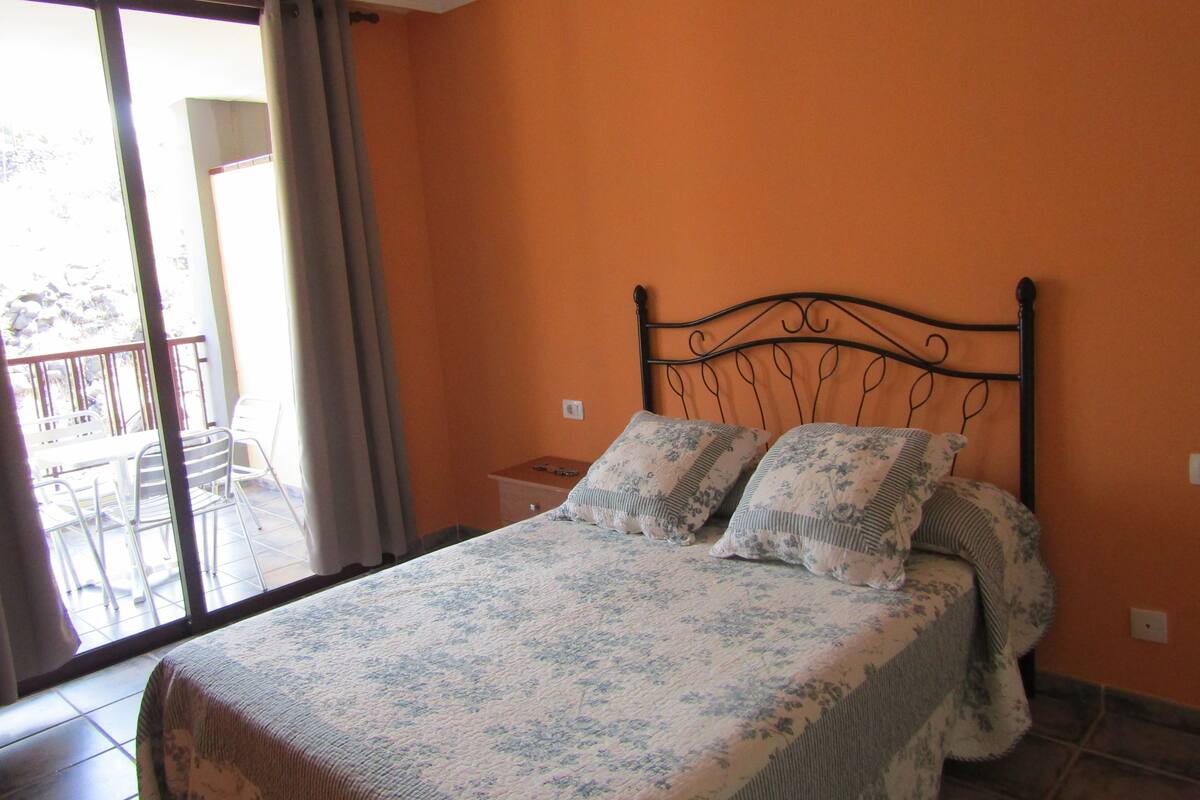 A bedroom with a bed, a nightstand, and a view of an outdoor balcony.