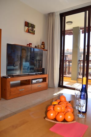 A living room with a television, a table with oranges, a bottle, and a window with curtains. - Olivia Sunbeach (Santiago del Teide)