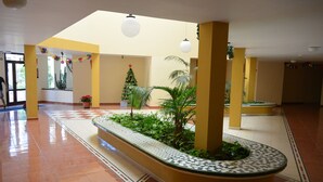 A spacious lobby with a tiled floor, a central planter with greenery, and a Christmas tree. - Olivia Sunbeach (Santiago del Teide)