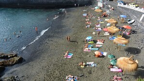 A beach with people sunbathing, umbrellas, and a rocky shoreline. - Olivia Sunbeach (Santiago del Teide)