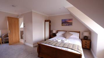 A bedroom with a wooden bed, a nightstand, a bedside table, a chair, and a painting on the wall.