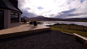 Ein modernes Haus mit einer Terrasse mit Blick auf einen See und Berge.