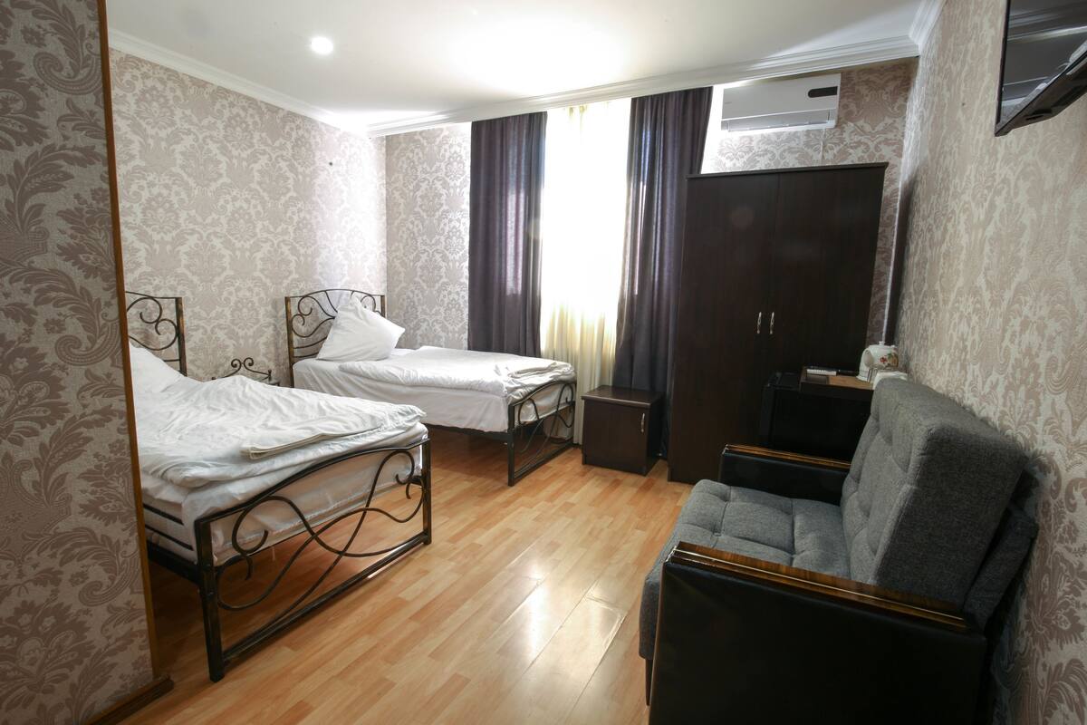 A bedroom with two single beds, a sofa, a wardrobe, and a TV.