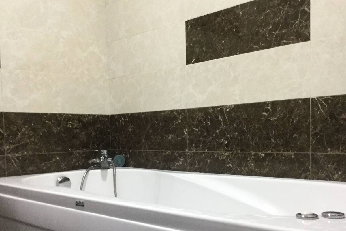 A modern bathroom with a large bathtub, dark marble tiles on the walls, and a white floor.