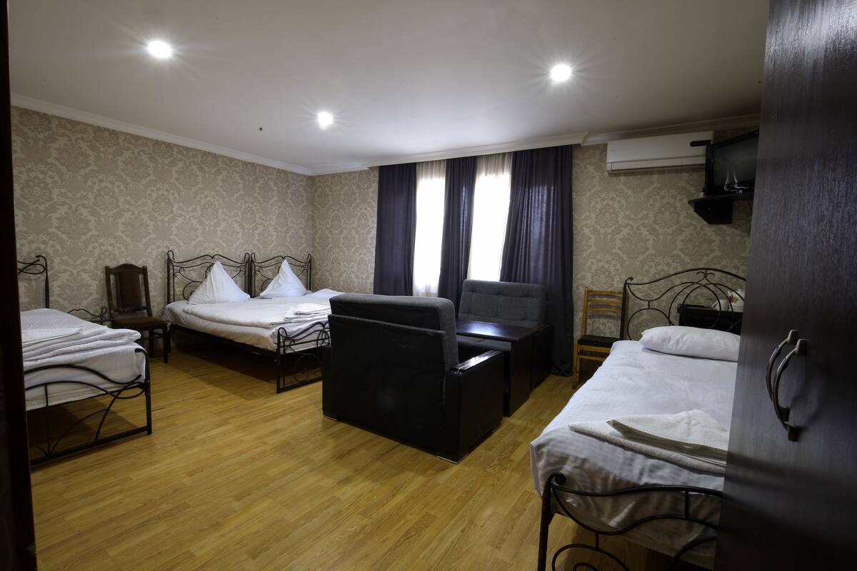 A hotel room with three single beds, a small sofa, a wooden chair, and a desk.