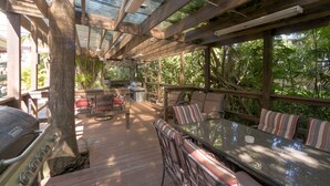 An outdoor patio with wooden furniture, a grill, and a view of lush greenery. - Villa 1 (Fort Lauderdale)