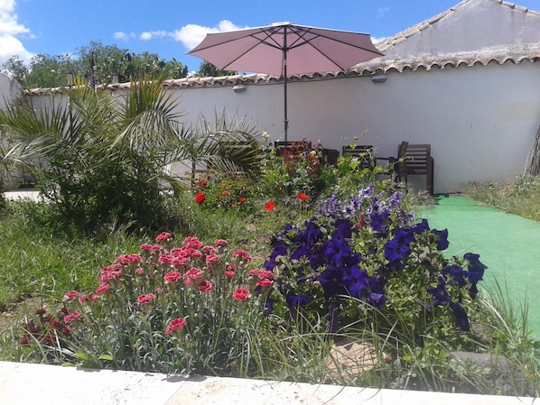 A garden with various flowers, a patio area with chairs, and a pergola with a canopy.