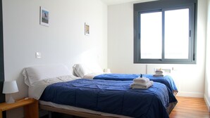 A bedroom with two beds, a nightstand with a lamp, and a window with blinds. - Casa Oretani (Picon)