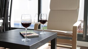 A table with two wine glasses and a magazine, a white chair, and a view of a pool through a window. - Casa Oretani (Picon)