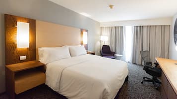 Habitación de hotel con una cama grande, un escritorio, una silla y una ventana con cortinas.