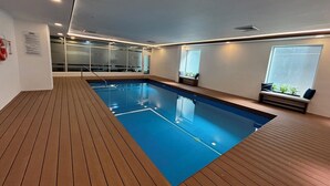 Une piscine intérieure moderne avec un sol en bois et des murs en verre.