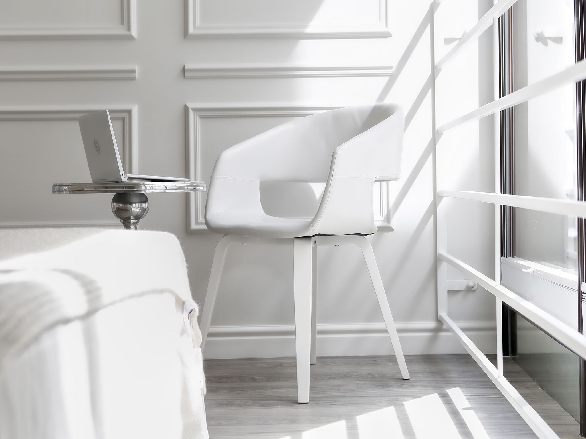 Une pièce moderne avec une chaise blanche, un ordinateur portable posé sur un support et une grande fenêtre.