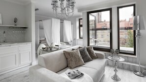 A modern living room with a sofa, a chandelier, and a view of the city through large windows. - Sweet Suite Apart (Gdansk)