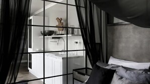 A bedroom with a large window, a bed with multiple pillows, and a view of a kitchen area. - Sweet Suite Apart (Gdansk)