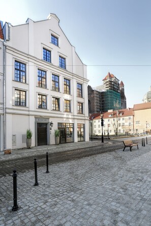 A cobblestone street with a white building featuring multiple windows and a sign that reads "Sweet Suite." - Sweet Suite Apart (Gdansk)