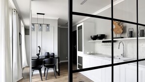 A modern kitchen with white cabinetry, a black countertop, and a wooden dining area with a black rug. - Sweet Suite Apart (Gdansk)