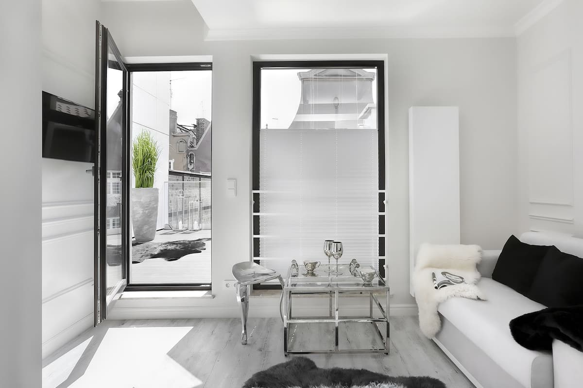 A modern living room with a glass door leading to a balcony, a sofa, a coffee table, and a TV mounted on the wall.