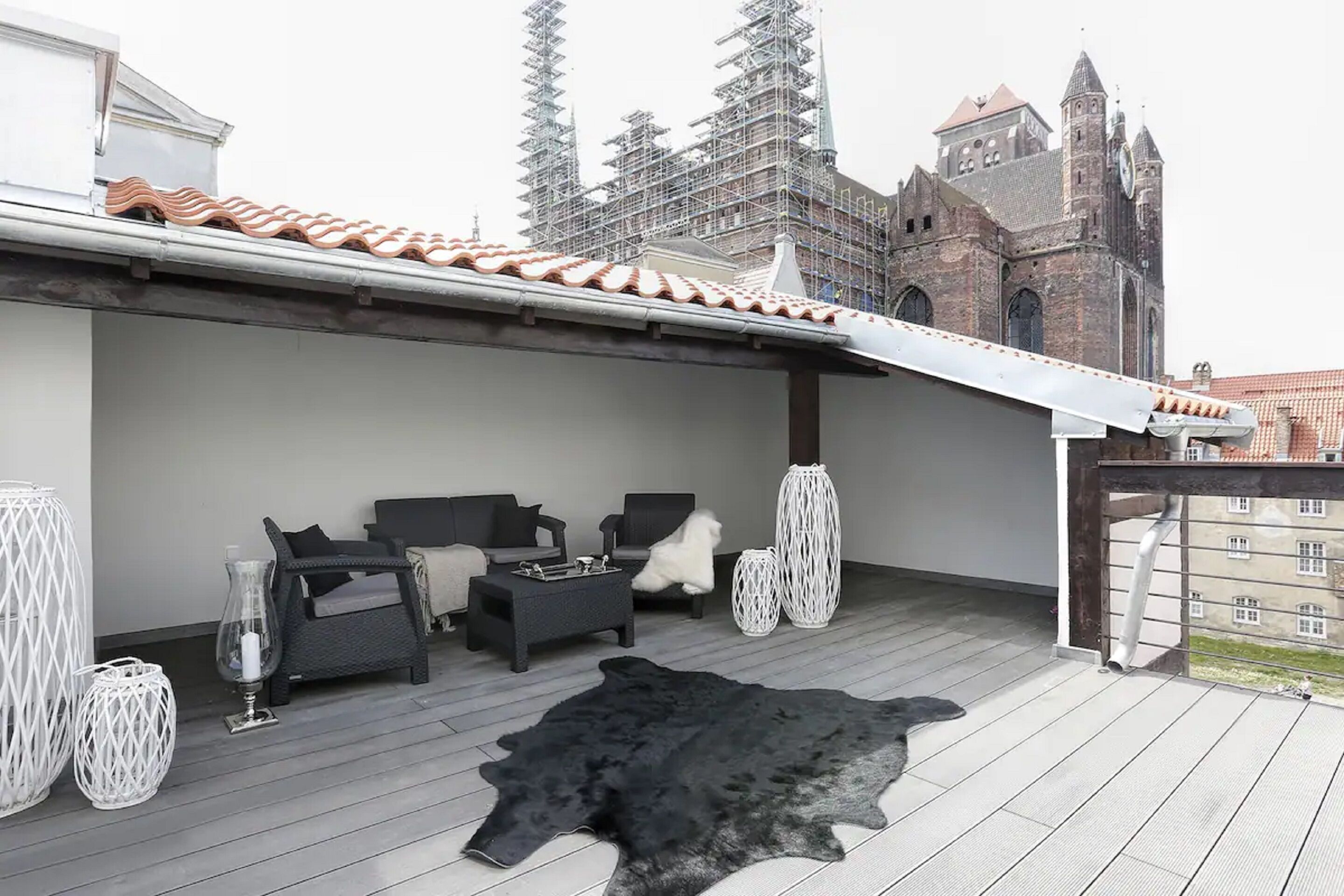 Een terras op het dak met een zwart leren vloerkleed, rieten meubels en witte vazen.