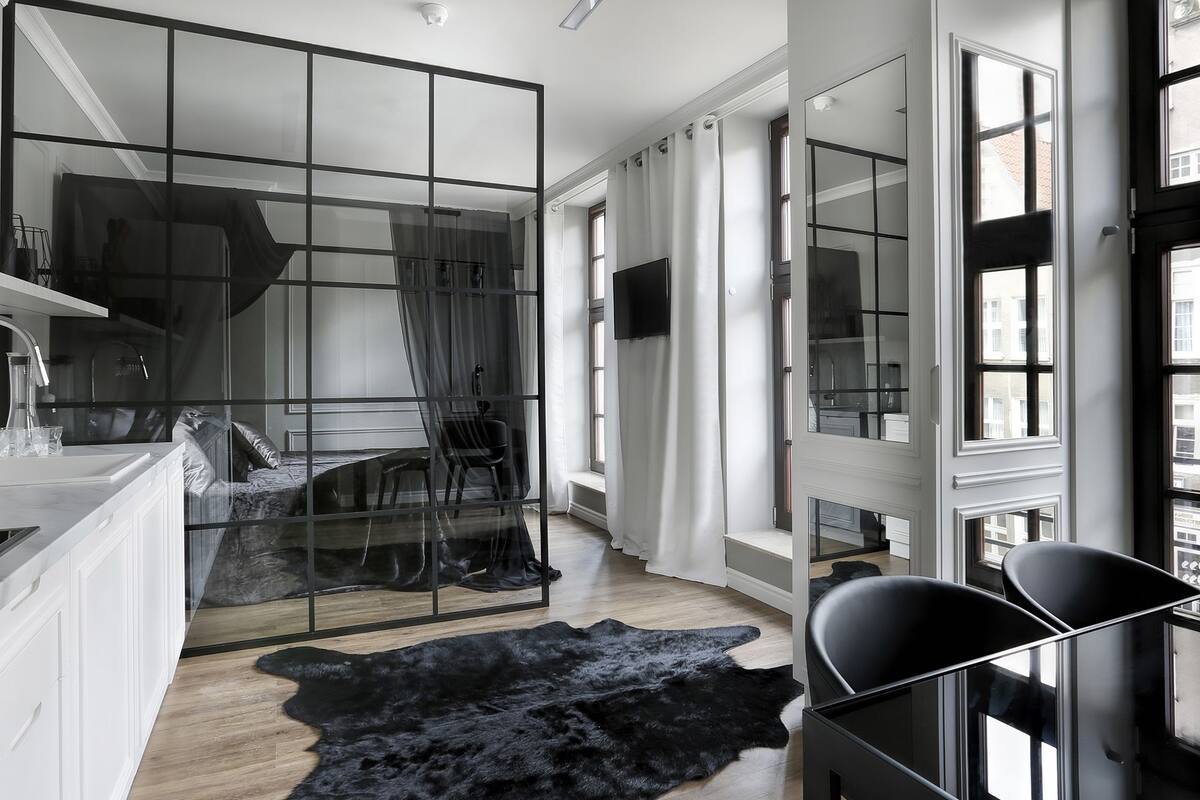 A modern room with a glass partition, a black leather sofa, a black leather chair, a black fur rug, and a television mounted on the wall.