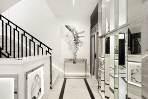 A modern hallway with a black railing, a marble floor, and a large abstract art piece on the wall.
