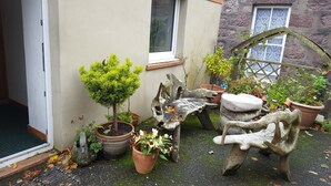 A small garden with potted plants, a wooden sculpture, and a stone bench. - Tower Guest House (Stornoway)