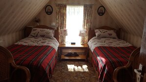 A cozy attic bedroom with two beds, floral curtains, and a small table with lamps. - Tower Guest House (Stornoway)