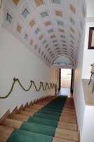 Una escalera con peldaños de color verde y marrón alternados, paredes blancas y un techo decorativo con diseños geométricos.