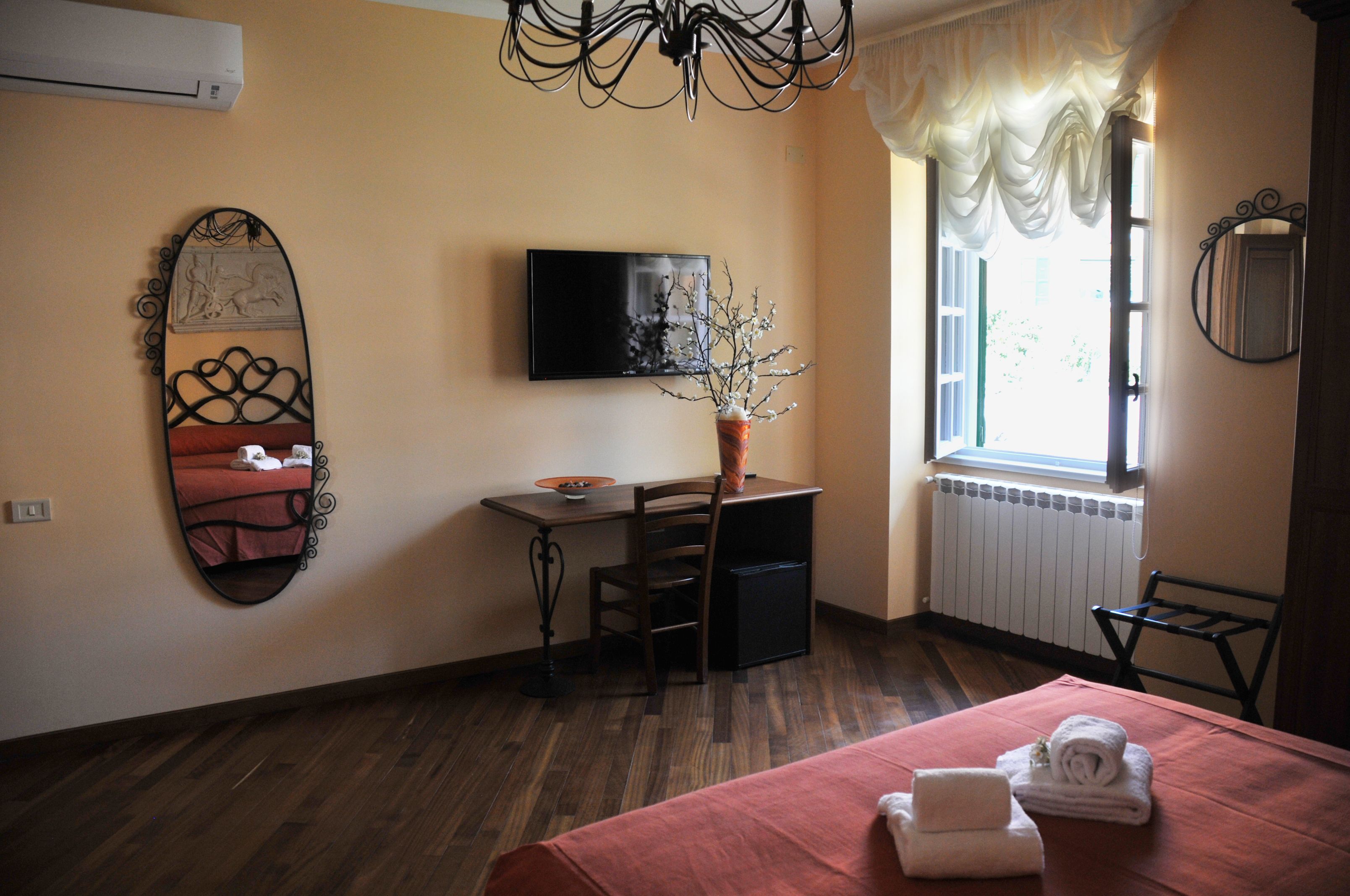 Una camera d'albergo con un letto, una scrivania, una sedia, una TV e una finestra con tende.