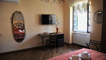 Una camera d'albergo con un letto, una scrivania, una sedia, una TV e una finestra con tende.