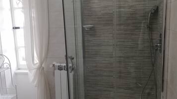 Een douche met glazen wanden, een betegelde vloer, een witte radiator en een metalen plankunit.