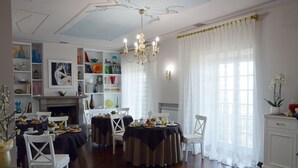 A dining area with round tables set for breakfast, white chairs, a chandelier, and a fireplace. - Antica Villa di Bruto (Tivoli)