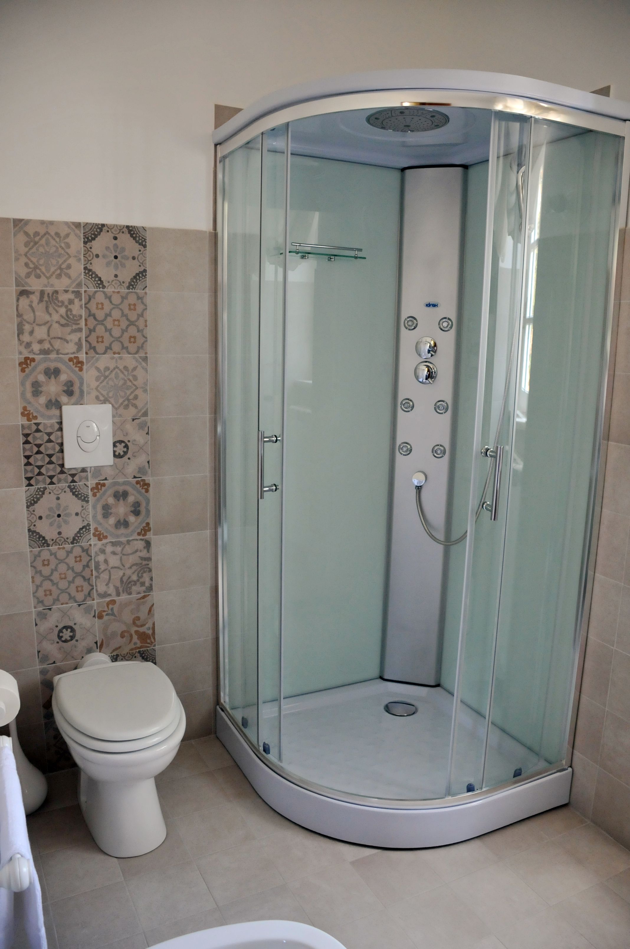A modern bathroom with a glass-enclosed shower, a toilet, and patterned tiles on the wall.