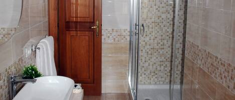 A bathroom with a bathtub, a shower enclosure, and a wooden door.