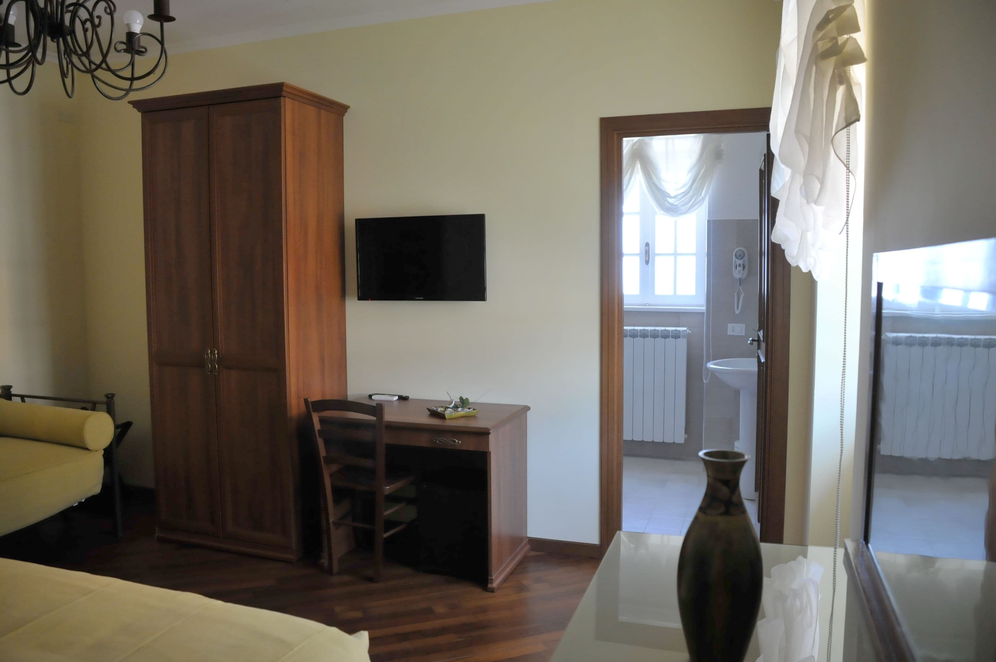 Una habitación con un armario de madera, un escritorio con una silla, televisión y un baño visible a través de una puerta abierta.