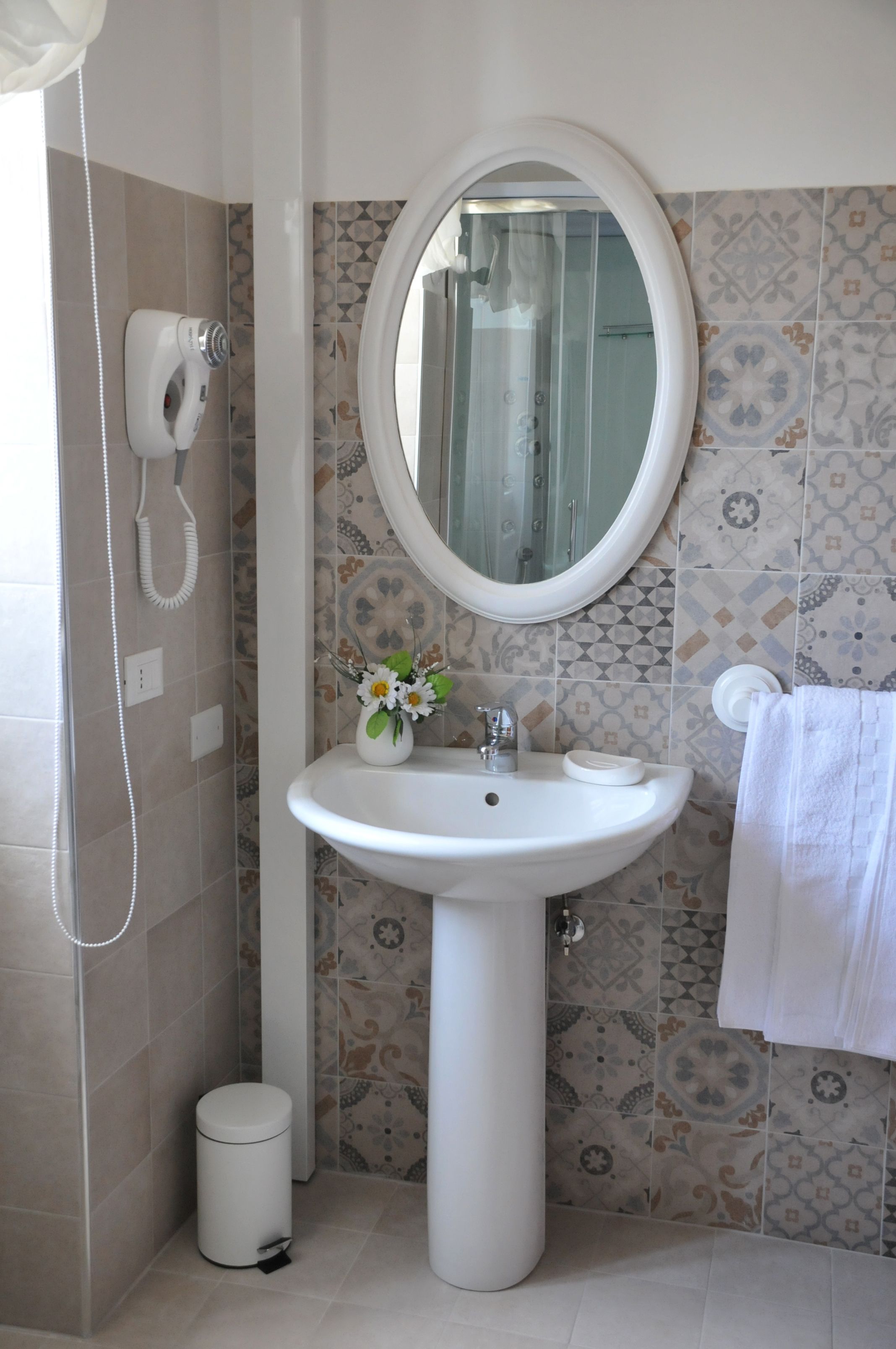 A bathroom with a pedestal sink, a mirror, a towel rack, and a hand dryer.