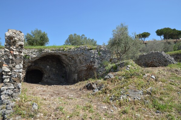 Une structure de pierre ancienne, dotée d’une entrée en forme de tunnel, entourée d’un terrain rocheux et d’une végétation clairsemée.