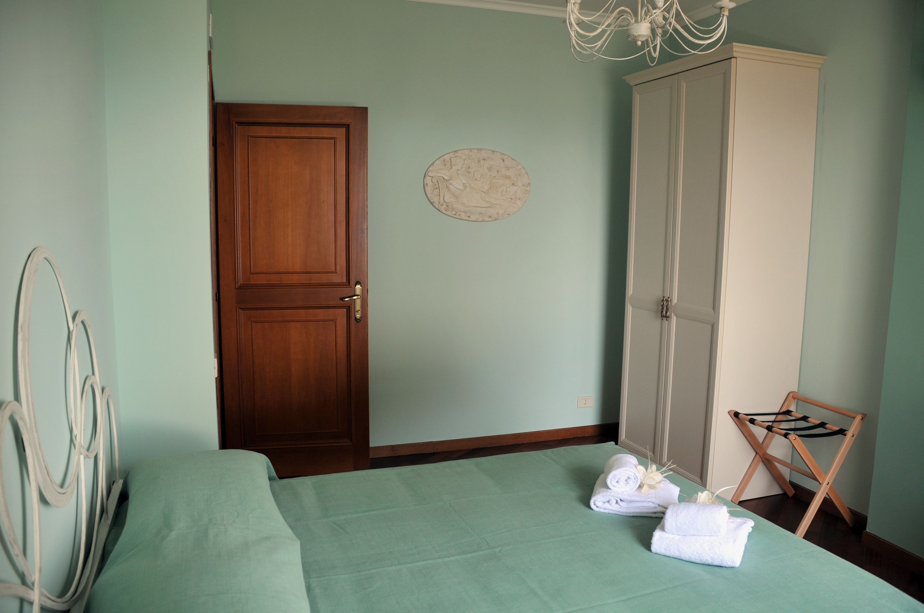 A bedroom with a bed, a wardrobe, a wooden door, a round wall decoration, and a folding chair.
