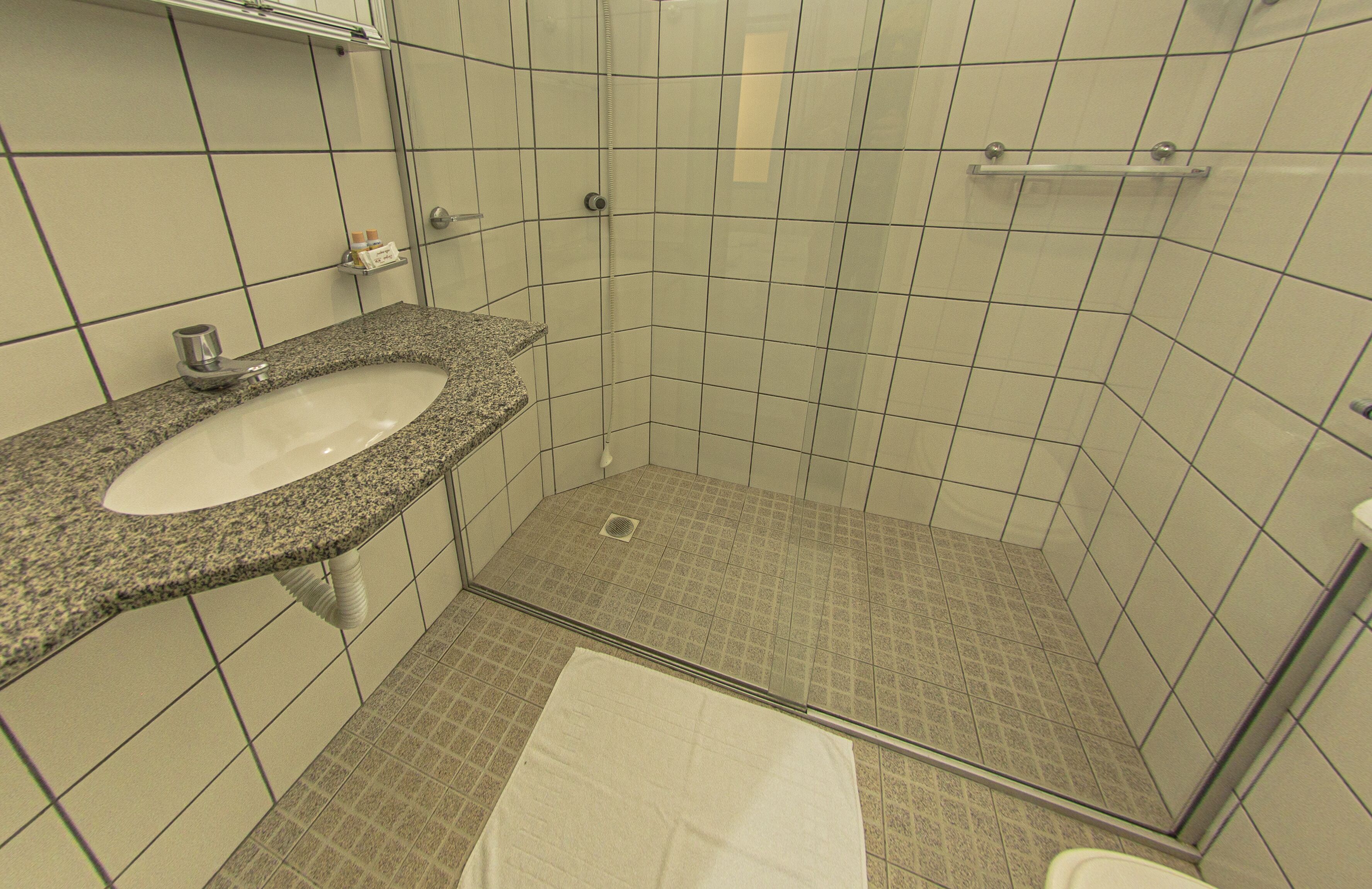 Un baño con lavamanos de encimera de granito, cabina de ducha con mampara de vidrio y suelo de baldosas.