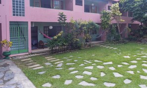 Un edificio rosa con un pequeño jardín que incluye piedras para caminar y una hamaca.
