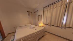 Une chambre d’hôtel avec un grand lit, une table de chevet avec une lampe et des rideaux aux fenêtres.