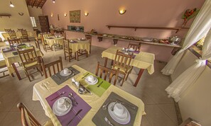Un comedor con varias mesas dispuestas para comidas, sillas y una barra con alimentos.