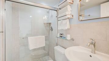 Un baño moderno con ducha de vidrio, inodoro blanco, lavabo con grifo cromado y espejo con marco dorado.